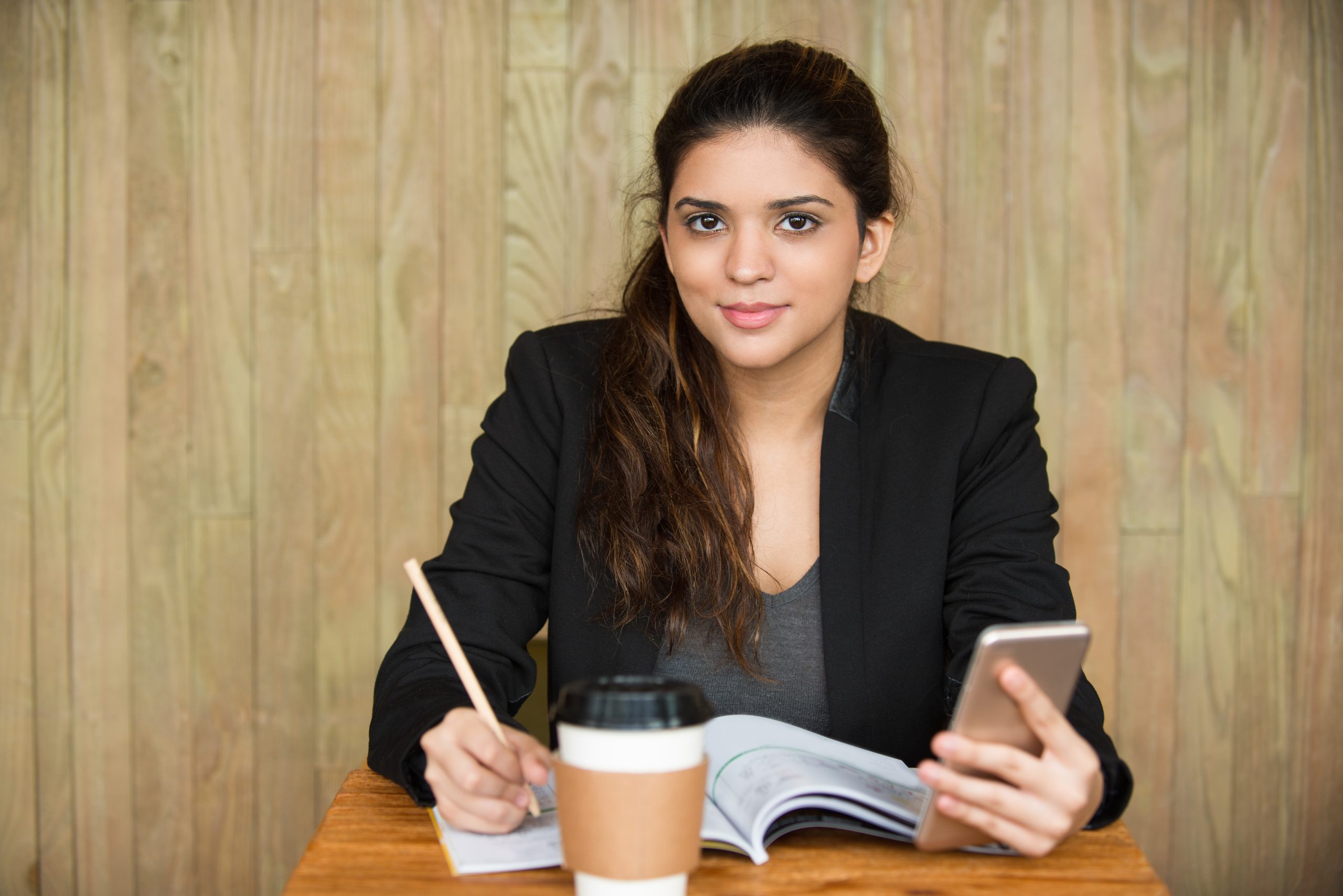 Portrait of young Caucasian female student sitting at desk, doing homework and networking on smartphone